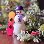 Handcrafted Seiffener Volkskunst Snowboarder snowman incense smoker wearing a purple helmet and scarf while holding a red snowboard, made in Seiffen, Germany.